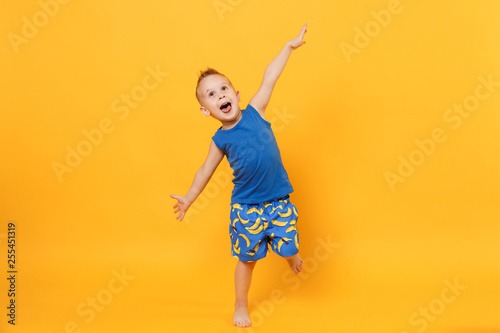 Smiling fun kid boy 3-4 years old wearing blue beach summer clothes isolated on bright yellow orange wall background, children studio portrait. People, childhood lifestyle concept. Mock up copy space.