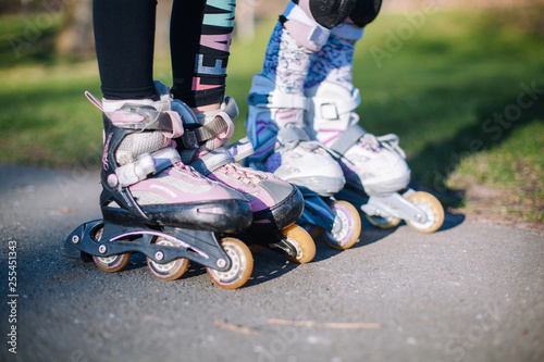 Two young girl standing on roller skates with protection on the knees in park and hold hands