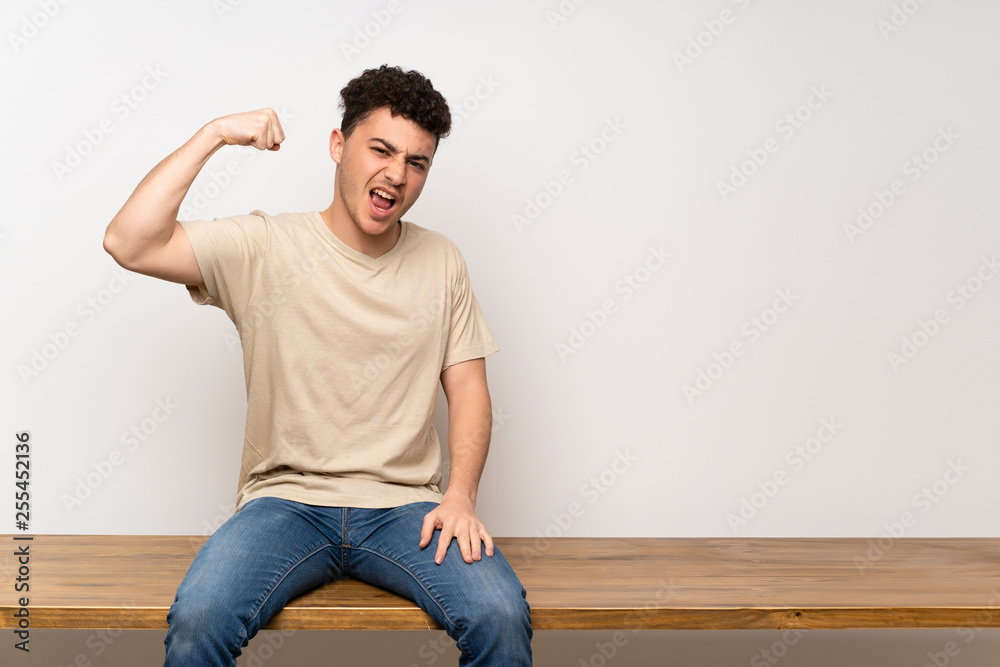 Young man sitting on table doing strong gesture Young man sitting on table doing strong gesture