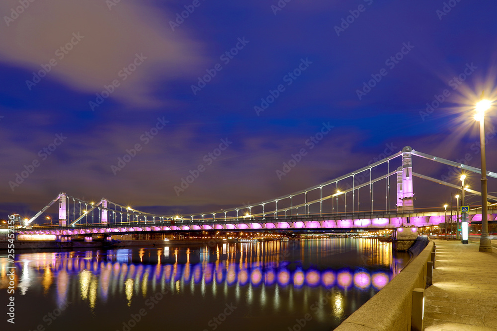 Fototapeta premium Krymsky Bridge or Crimean Bridge across the Moskva river in Moscow in the rays of setting sun in the evening blue hour with illumination