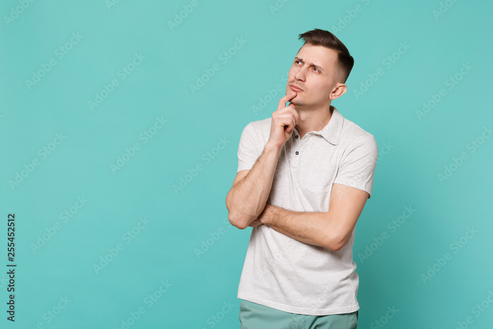 Portrait of thinkful young man in casual clothes looking up, put hand prop up on chin isolated on blue turquoise background in studio. People sincere emotions, lifestyle concept. Mock up copy space. Portrait of thinkful young man in casual clothes looking up, put hand prop up on chin isolated on blue turquoise background in studio. People sincere emotions, lifestyle concept. Mock up copy space.