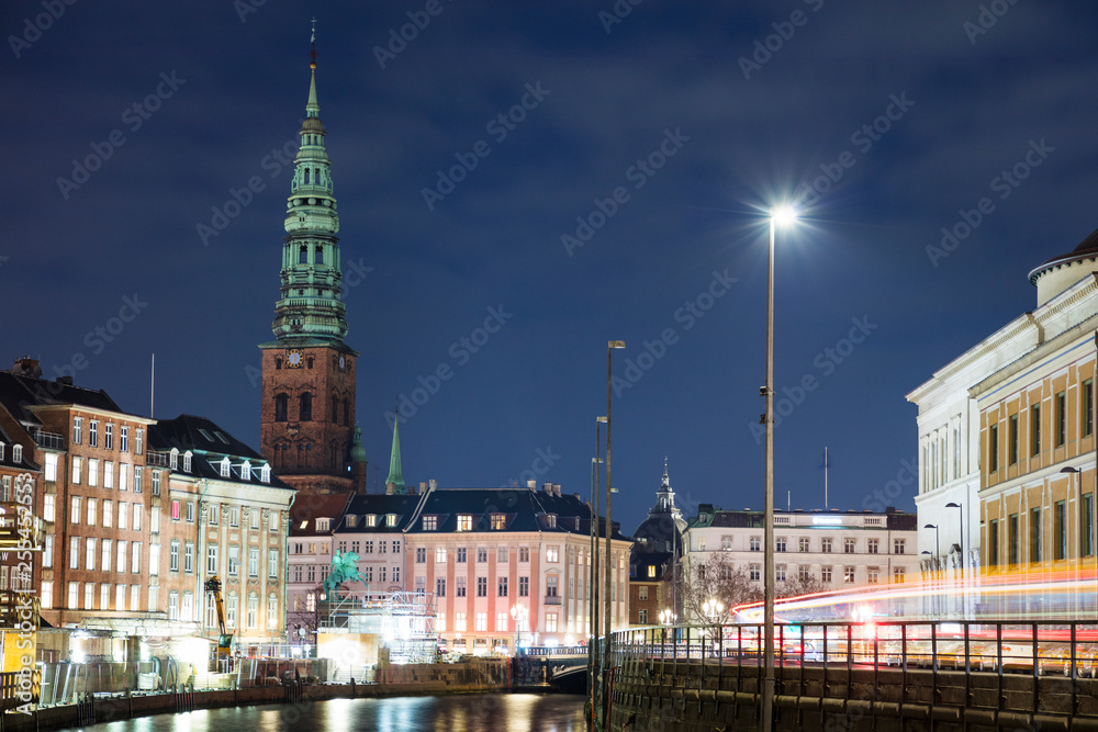 High tower of castle behind buildings and canal in night lights in Copenhagen in Denmark