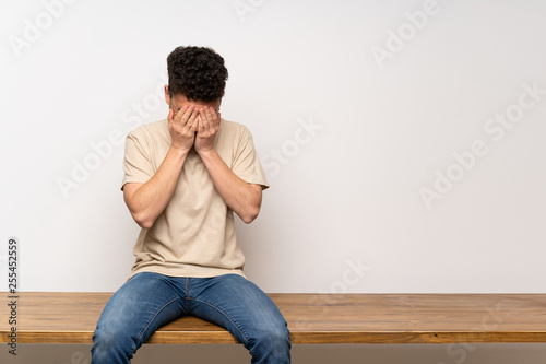Young man sitting on table with tired and sick expression