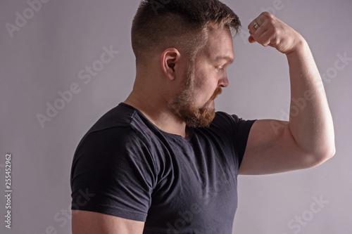 Portrait of attractive young sporty man in black t-shirt standing with arm up, showing muscles isolated on gray background. Hard light