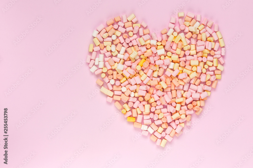 Top view of the multi-colored marshmallows which lies in the shape of a heart on a monochrome pink background copyspace, topview, mockup, flatlay