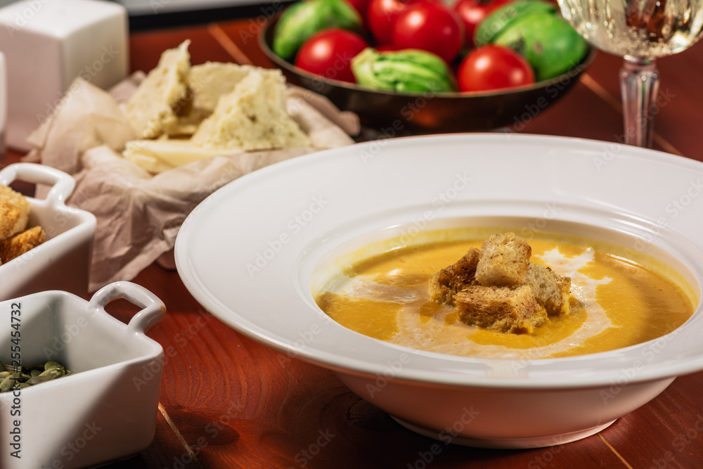 Roasted pumpkin and carrot soup with cream, pumpkin seeds. Served with croutons, cheese and white wine on wooden background. Copy space Roasted pumpkin and carrot soup with cream, pumpkin seeds. Served with croutons, cheese and white wine on wooden background. Copy space