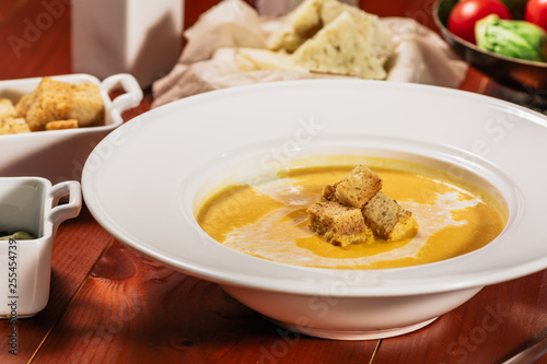 Dietary vegetarian pumpkin cream soup puree, served with white wine, pumpkin seeds, cheese and croutons, on brown wooden table, close up.