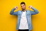 Handsome man over yellow wall showing thumb down
