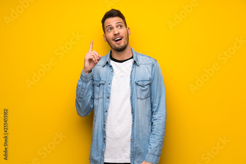 Handsome man over yellow wall intending to realizes the solution while lifting a finger up