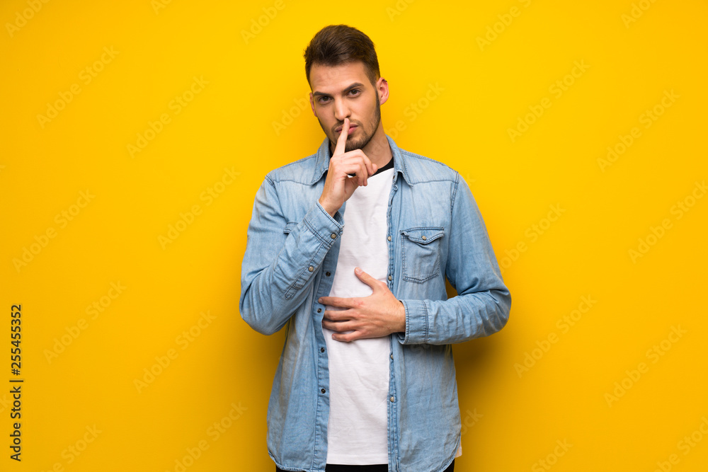 Handsome man over yellow wall showing a sign of silence gesture putting finger in mouth Handsome man over yellow wall showing a sign of silence gesture putting finger in mouth