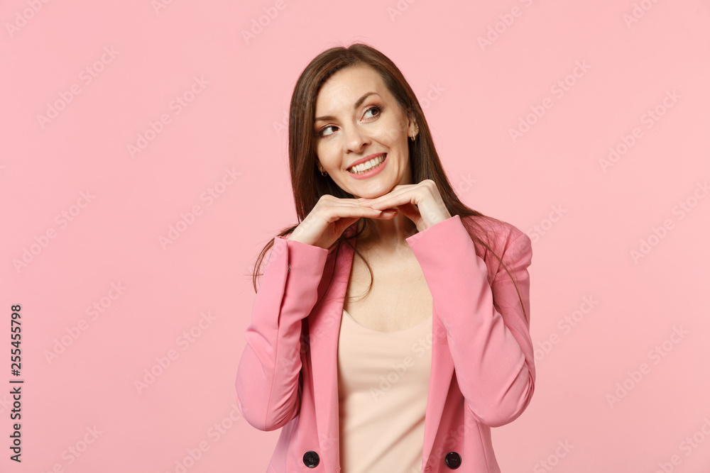 Portrait of smiling young woman wearing jacket put hand prop up on chin looking aside isolated on pastel pink wall background in studio. People sincere emotions, lifestyle concept. Mock up copy space. Portrait of smiling young woman wearing jacket put hand prop up on chin looking aside isolated on pastel pink wall background in studio. People sincere emotions, lifestyle concept. Mock up copy space.