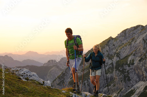 Photography Hiker couple trekking up a grassy hill in the picturesque Alps at sunrise