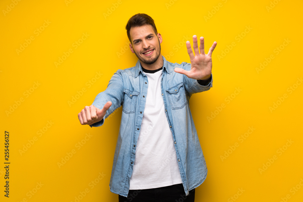 Handsome man over yellow wall counting six with fingers Handsome man over yellow wall counting six with fingers