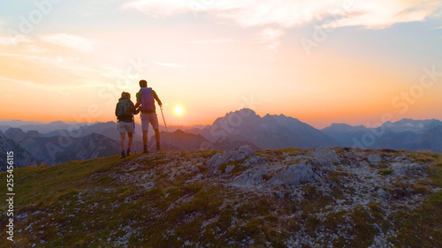 AERIAL: Unrecognizable hiker couple observes evening landscape from mountaintop. © helivideo