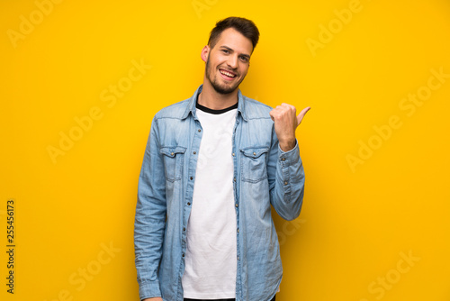 Handsome man over yellow wall pointing to the side to present a product