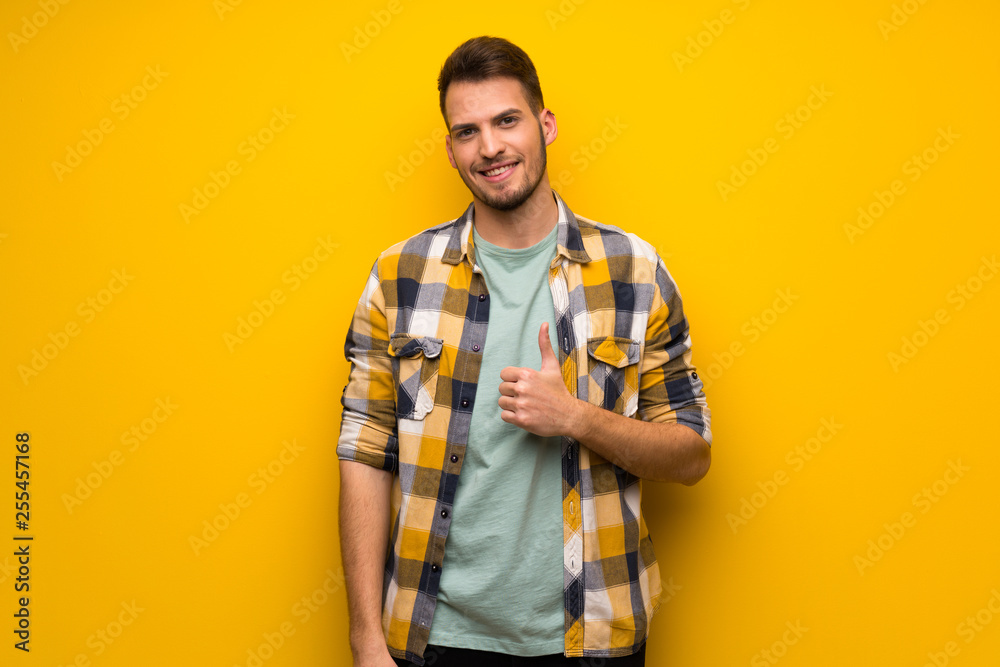 Handsome man over yellow wall giving a thumbs up gesture and smiling Handsome man over yellow wall giving a thumbs up gesture and smiling