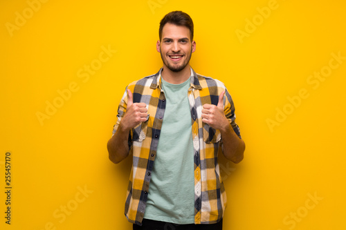 Handsome man over yellow wall with thumbs up because something good has happened