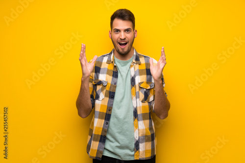 Handsome man over yellow wall with shocked facial expression