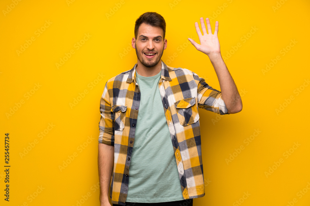 Handsome man over yellow wall saluting with hand with happy expression Handsome man over yellow wall saluting with hand with happy expression