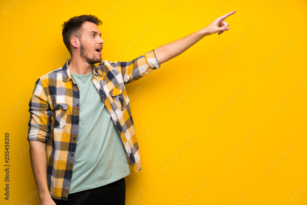 Handsome man over yellow wall pointing away Handsome man over yellow wall pointing away