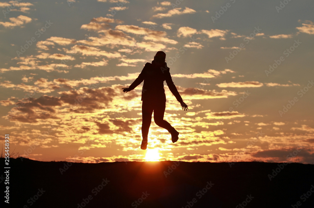 Silhouette of a happy girl jumping into the sky against the backdrop of an incredible sunset, sky and clouds