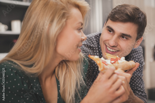 Close up of a happy beautiful woman smiling at her handsome man  eating delicious pizza at home. Handsome man watching his lovely girlfriend eating tasty pizza. Romance  care  family concept