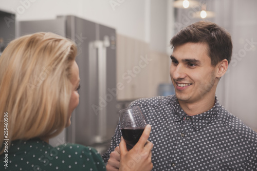 Attractive young man enjoying wine with his wife at home. Happy man smiling, talking to his grlfriend, resting at home with a glass of wine. Valentines day, celebration, holidays concept photo