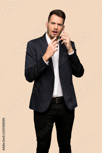 Handsome business man nervous and scared putting hands to mouth over ocher background