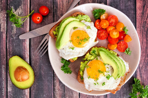 Avocado toasts with eggs and tomatoes on whole grain bread. Above view on a dark wood background.