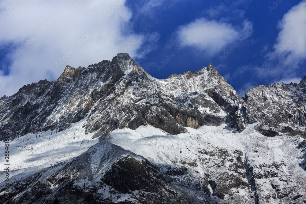 Fototapeta premium ShuangQiao Valley Scenic Area, Siguniangshan - Four Girls Mountain National Park in Sichuan Province, China. Snow Capped Jagged Mountains with clouds forming at the summit. Blue Sky, Snow Mountains