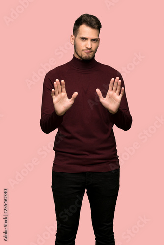 Man with turtleneck sweater making stop gesture and disappointed over pink background © luismolinero
