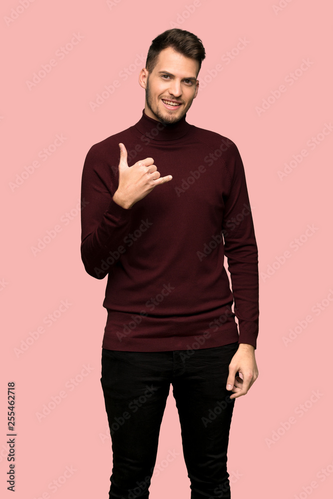 Man with turtleneck sweater making phone gesture. Call me back sign over pink background Man with turtleneck sweater making phone gesture. Call me back sign over pink background