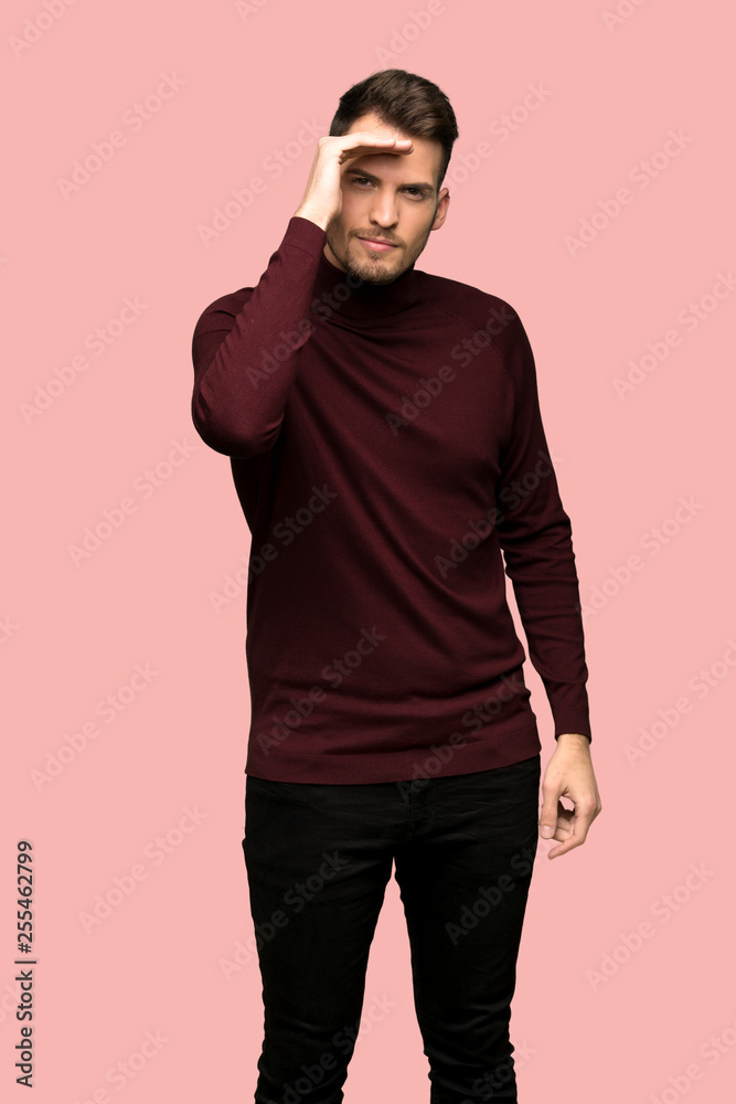 Man with turtleneck sweater looking far away with hand to look something over pink background Man with turtleneck sweater looking far away with hand to look something over pink background