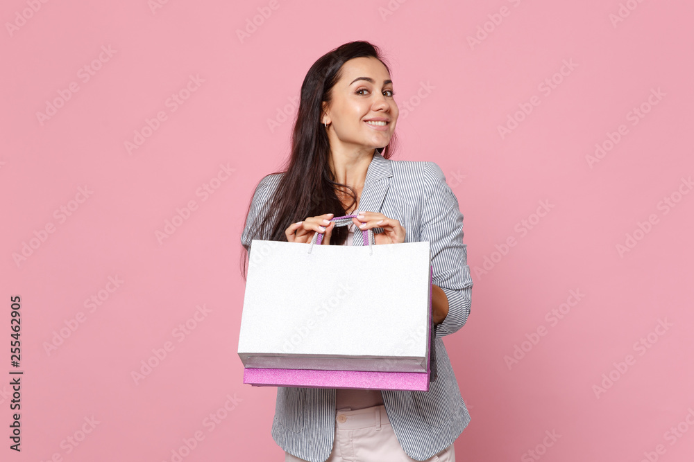 Smiling young woman in striped jacket looking aside holding package bag with purchases after shopping isolated on pink pastel background. People sincere emotions lifestyle concept. Mock up copy space. Smiling young woman in striped jacket looking aside holding package bag with purchases after shopping isolated on pink pastel background. People sincere emotions lifestyle concept. Mock up copy space.