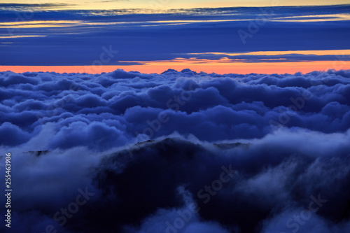 Abstract photograph above the clouds, sea of clouds effect, flying through the sky, aerial view, puffy clouds, orange sunset sky. Low pressure front atmospheric effect, cloudscape, clear weather.