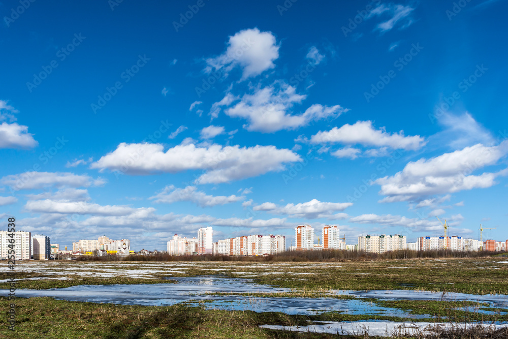 view of the field with a frozen pond and the outskirts of the city, new city under construction, spring sunny day