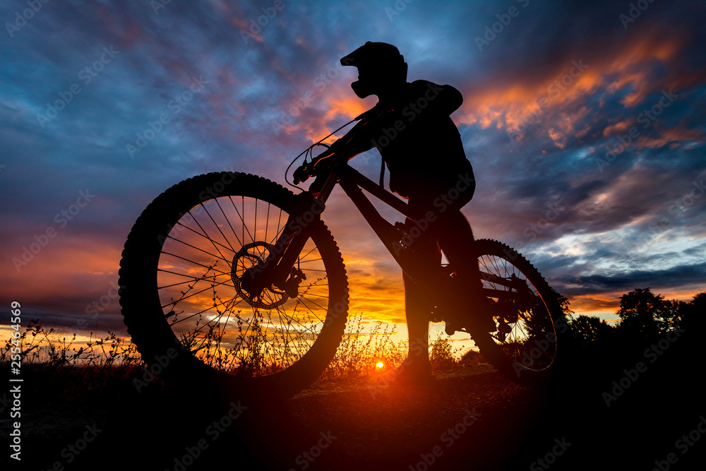 Downhill mountain bike rider silhouette at sunset with full face helmet