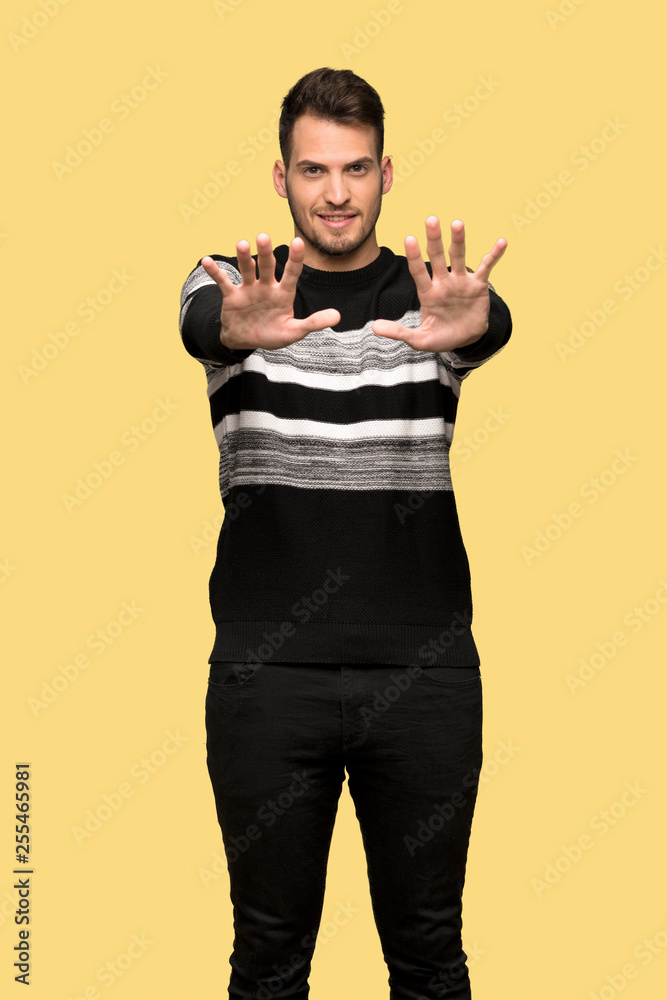 Handsome man counting ten with fingers over yellow background