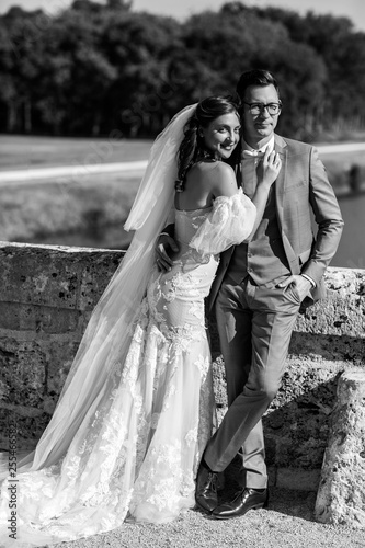 Attractive young modern newlyweds in stylish wedding clothes hugging outdoors in their wedding day. Black and white photo