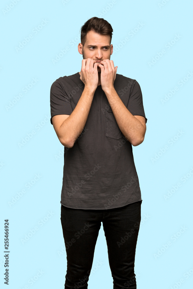 Man with black shirt nervous and scared putting hands to mouth over blue background Man with black shirt nervous and scared putting hands to mouth over blue background