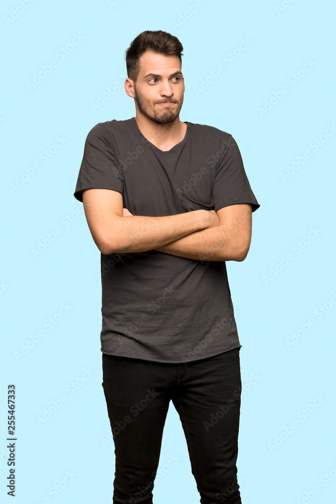 Man with black shirt making doubts gesture while lifting the shoulders over blue background Man with black shirt making doubts gesture while lifting the shoulders over blue background