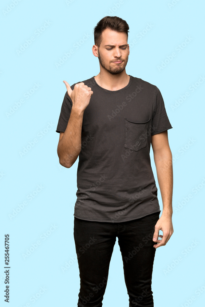 Man with black shirt unhappy and pointing to the side over blue background Man with black shirt unhappy and pointing to the side over blue background