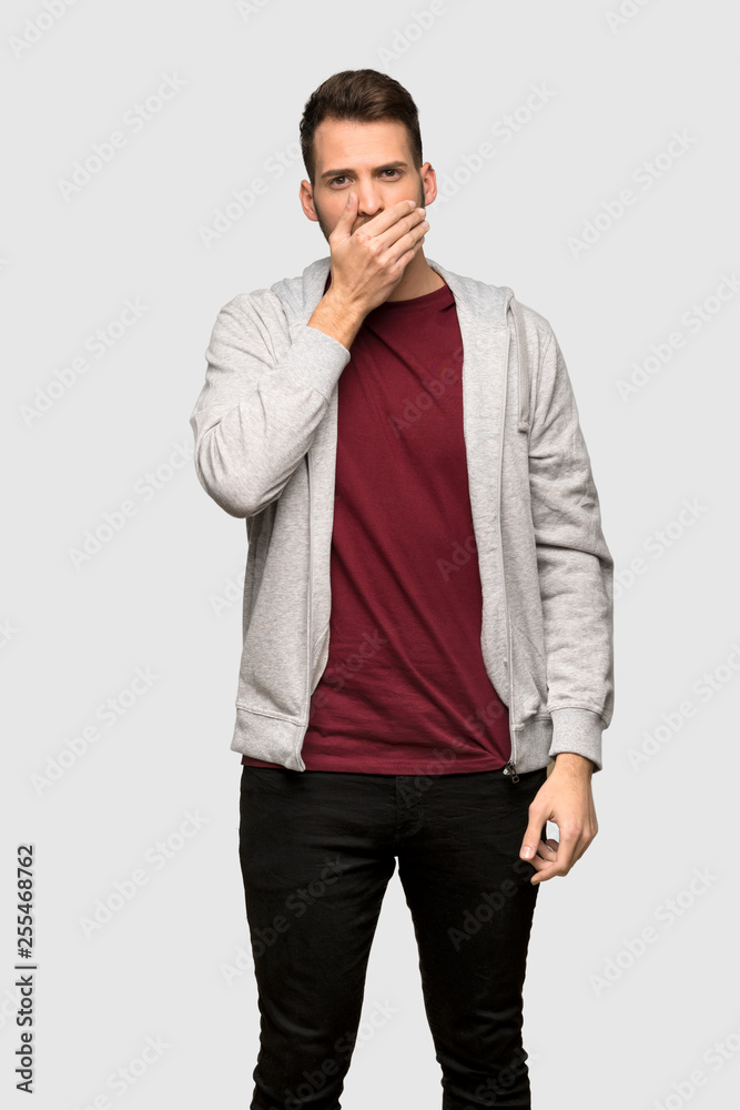 Man with sweatshirt covering mouth with hands for saying something inappropriate over grey background Man with sweatshirt covering mouth with hands for saying something inappropriate over grey background