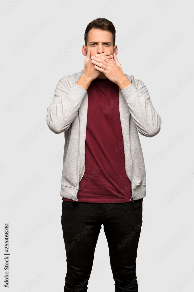 Man with sweatshirt covering mouth with hands for saying something inappropriate over grey background Man with sweatshirt covering mouth with hands for saying something inappropriate over grey background