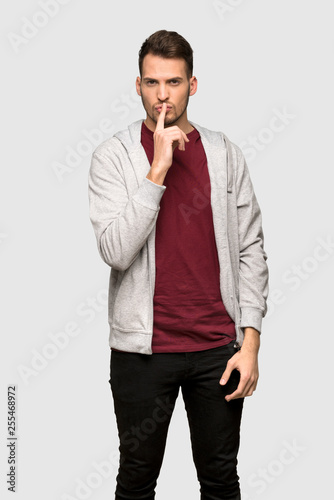 Man with sweatshirt showing a sign of silence gesture putting finger in mouth over grey background
