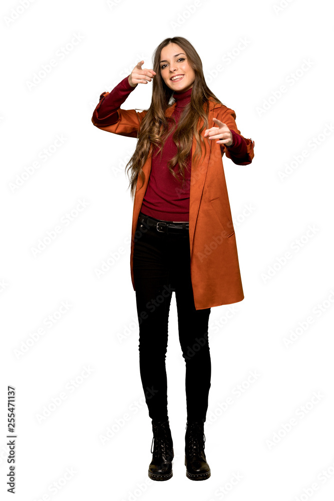 Full-length shot of Young woman with coat points finger at you while smiling on isolated white background Full-length shot of Young woman with coat points finger at you while smiling on isolated white background