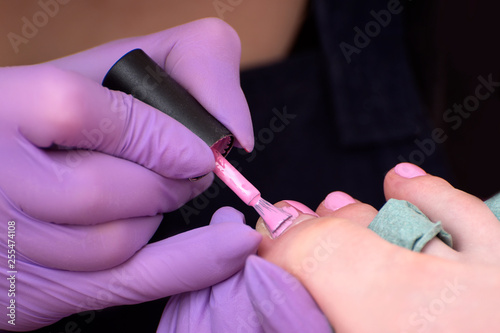 Covering toenails with pink nail polish. Close-up. Manicure salon