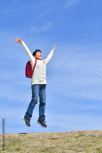 青空でジャンプする小学生の女の子（ランドセル） © hanapon1002
