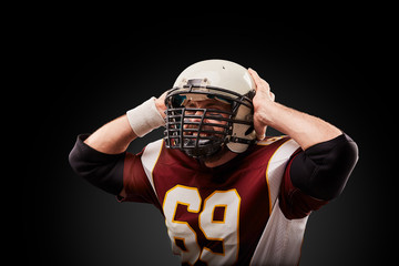 American football player in a helmet holding his head in pain against a black background
