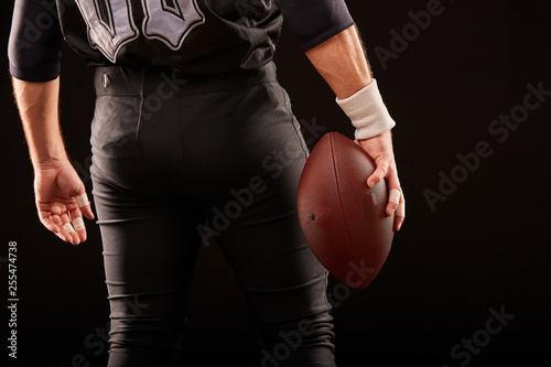 Mid section of American football player with ball against black, copy space, back view © Georgii
